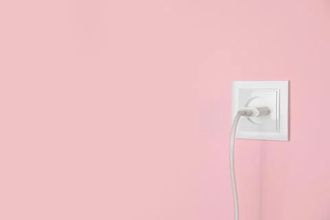 Charger adapter plugged into power socket on pink wall, space for text. Elect Stock Photos