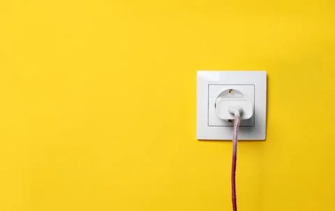 Charger adapter plugged into power socket on yellow wall, space for text. E.. Stock Photos