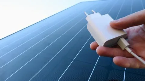 Charger for mobile devices in hand on the background of a solar panel. The .. Stock Photos