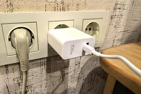 Charger plugged into wall socket with cable connected to device on wooden table Stock Photos