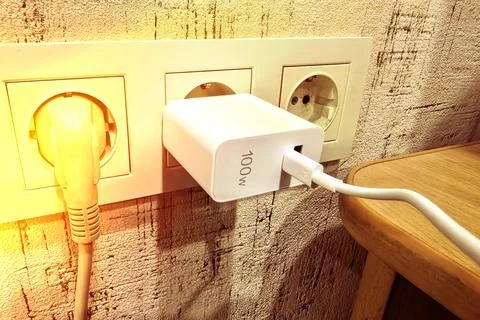 Charger plugged into wall socket with cable connected to device on wooden table Stock Photos