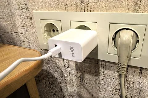 Charger plugged into wall socket with cable connected to device on wooden table Stock Photos