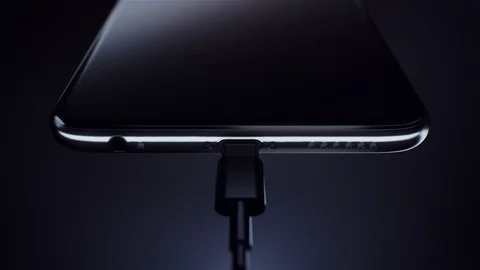 Charging a black smart phone using a cable. Green battery icon. Visualization of Vídeos de archivo 128363552