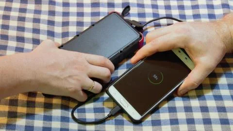 Charging a cell mobile phone with someone elses solar power bank and cable Stock Photos