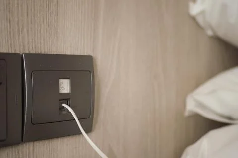 Charging device connected to wall socket near bed Stock Photos