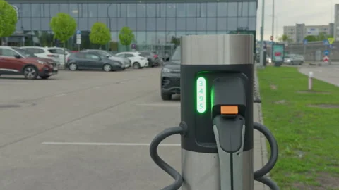 Charging point by office parking. Electric vehicle charging hub amidst cityscape Stock Footage 335684553