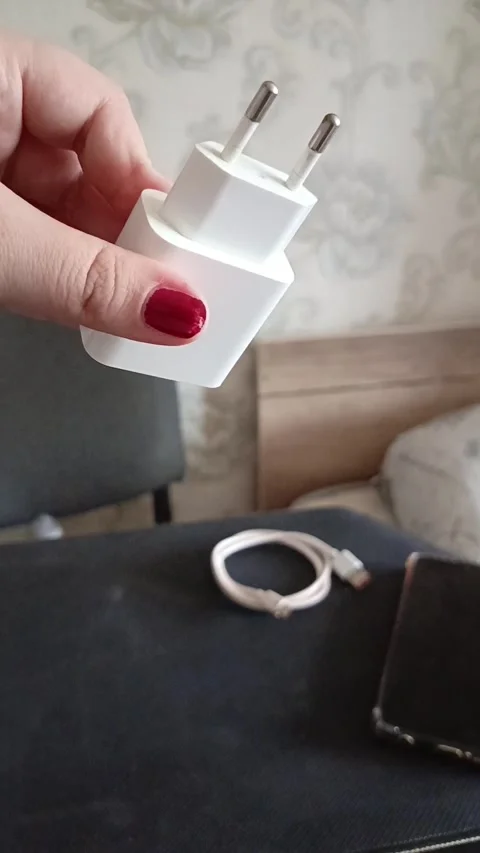 A charging unit in a womans hand, a cable and a phone on the table. Phone Stock Footage 319980601