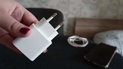 A charging unit in a womans hand, a cable and a phone on the table. Phone Video stock 319980619