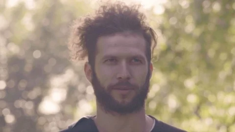 Charismatic bearded man looking in camera and then smiling in sunshining summer Stock Footage 98726559