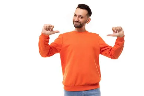 Charismatic bearded man in orange sweater points thumbs at himself, leadership Stock Photos