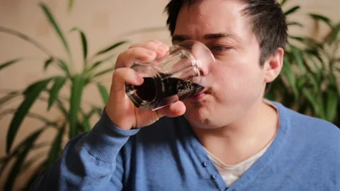 A charismatic guy in a blue sweater drinks soda from a glass glass Stock-Footage 149314946