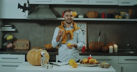 Charismatic man juggling with some oranges in his kitchen ,at his table , in Stock Footage 96416607