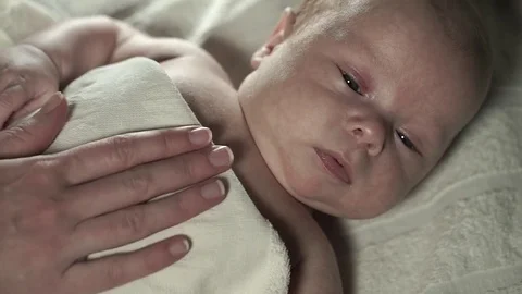A charming baby lying on a bed under a blanket. Mother strokes it. Stock Footage 73179944