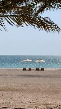 Charming beach with two sun beds facing shining water, surrounded by palm trees Stock Photos