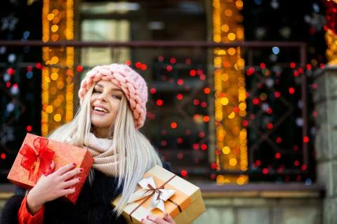 Charming blonde model dressed in warm outfit, holding gift boxes at the backg Stock Photos
