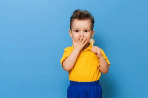 A charming boy looks at the camera while holding a lollipop on a blue background Stock Photos