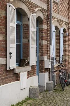 Charming brick building featuring open shutters, a window, and bicycles resti Stock Photos