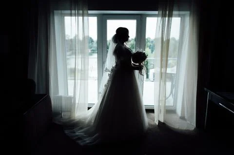 Charming bride stand in front of window. Girl stand by the window at her room Foto stock