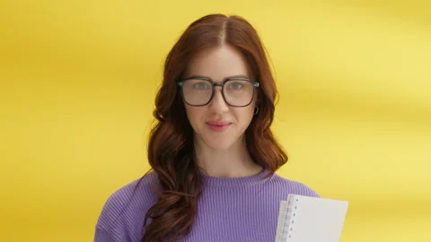 Charming brunette in big glasses biting lip seductively, holding notebooks Video stock 245838239