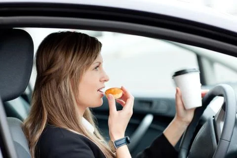 Charming businesswoman eating and holding a drinking cup while driving Stock Photos