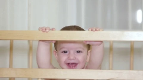 A charming child in a crib laughs and claps her hands and at the same time tries Stock Footage 79470042