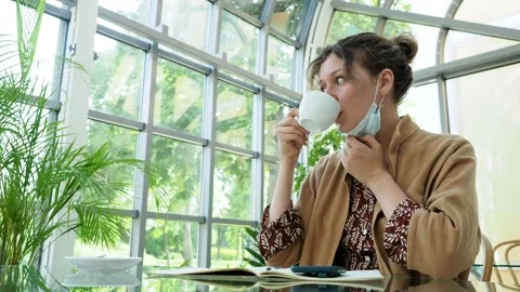 Charming curly dark haired lady takes off protective mask to drink fresh coffee 库存影片 147405019