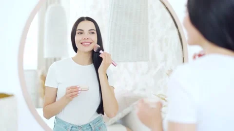 Charming dark haired lady apply blush powder on cheek using makeup brush looking Stock Footage 221828630