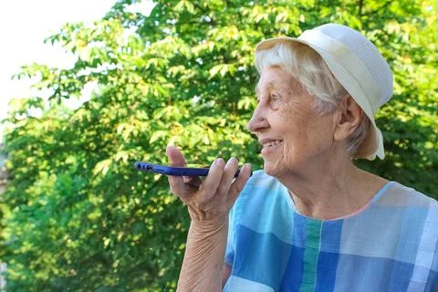 Charming elderly woman in rectangular black rimmed eyewear using voice recogn Stock Photos