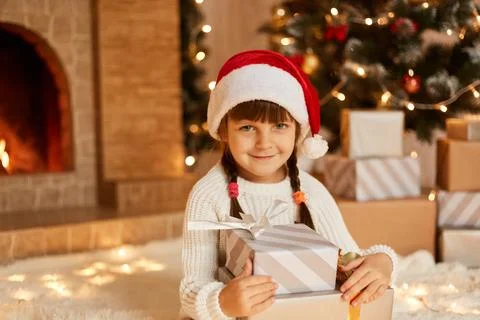 Charming female kid holding stack of present, little kid wearing white sweate Stock Photos
