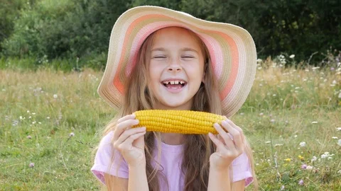 A charming girl eats fragrant corn wearing summer hat. Stock Footage 113085322