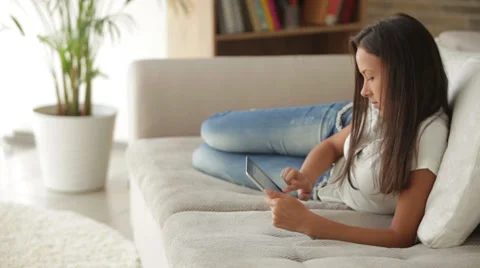 Charming girl lying on sofa using touchpad and smiling Vídeos de archivo 34196931