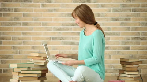 Charming girl sitting on floor with stack of book using laptop looking at camera Stock Footage 33851133