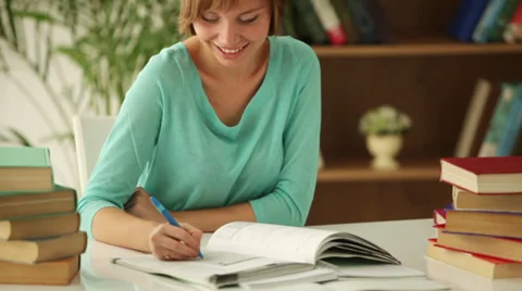 Charming girl sitting at table studying writing in notebook looking at camera Stock Footage 33851247