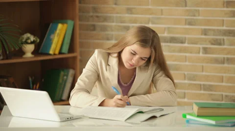 Charming girl sitting at table studying writing in workbook looking at camera Stock Footage 34114868