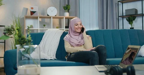 Charming happy satisfied young arabic woman in headscarf sitting on soft couch Stock Footage 150112184