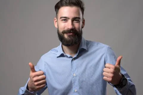 Charming happy young bearded smart casual man showing thumbs up hand gesture  Stock Photos