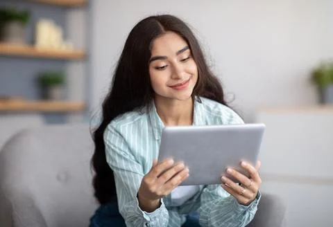 Charming Indian lady using tablet computer, studying remotely or having online Стоковые фото