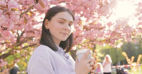 Charming lady drinking coffee and resting in blooming garden at sunny day. Video stock 129115491