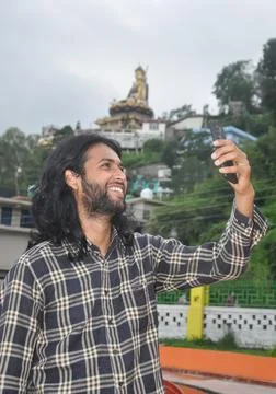 A charming long haired and bearded young guy smiling with taking selfie Stock Photos