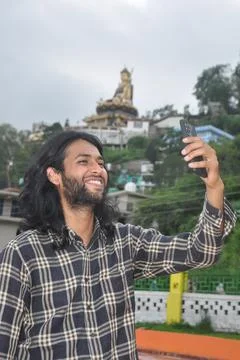 A charming long haired and bearded young guy smiling with taking selfie Foto stock