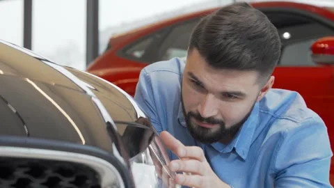 Charming man examining a sleek new car at the dealership with a confident smile Stock Footage 311986407