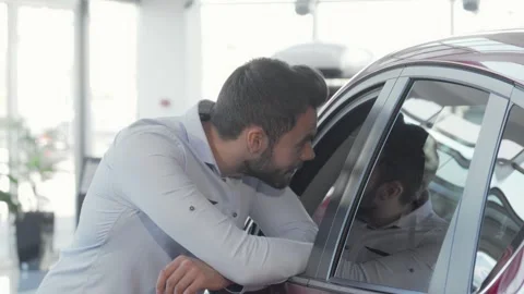 Charming man smiling at the camera while inspecting a car at the dealership Stock Footage 311944838