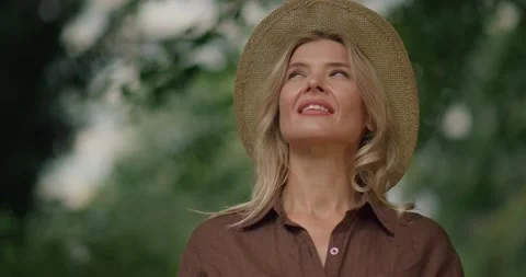 Charming Middle-Aged Lady in a Straw Hat and Casual Shirt enjoys Nature at Park Video stock 162036959