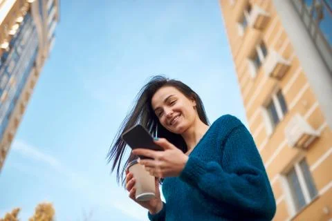 Charming model posing with a cellphone opposite modern towers and sky Foto stock