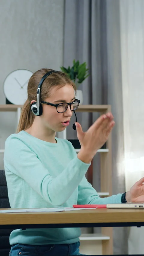 Charming positive smart 20-aged light haired girl in headphones sitting at the t Stock Footage 332739807