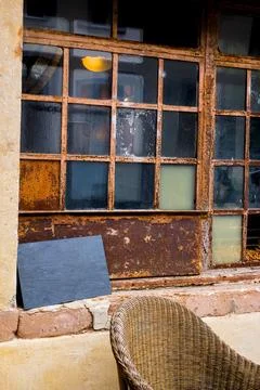 Charming rustic guesthouse with rusted window, empty slate, wicker chair. Stock Photos