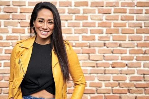 Charming smiling Hispanic woman near brick wall in city Stock Photos