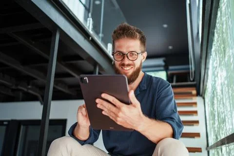 A Charming Smiling Man Engaged with a Tablet in a Modern Home Environment Stock Photos