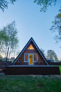 Charming triangular cabin with warm lights nestled among trees during twili.. Foto stock