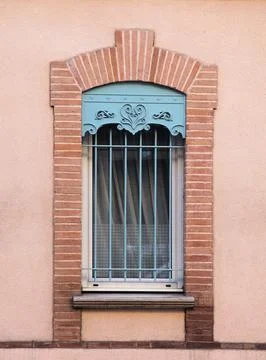 A charming window framed by rustic bricks features intricate iron bars and a  Stock Photos